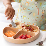 A child eats spaghetti from a Bumkins Silicone Grip Dish: Wood Grain with sections, wearing a patterned bib.