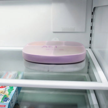 The Lavender Bumkins Silicone Grip Dish with Lid is on the fridge shelf, ideal for toddler portions.