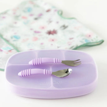 Bumkins Lavender Silicone Grip Dish with Lid and cutlery for toddlers, staged on pastel floral fabric.