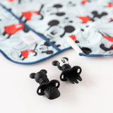 Two black Mickey Mouse Chewtensils® from the Bumkins Disney Little Ones Gift Bundle rest on a Mickey-themed cloth.