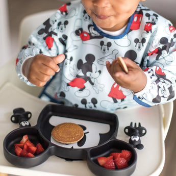 Child enjoying a pancake and strawberries from the Disney Little Ones Gift Bundle with Bib by Bumkins, featuring Mickey Mouse prints.