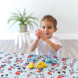 A child molds clay on a Disney Little Ones Mickey Mouse cloth by Bumkins, with a plant adding greenery in the background.