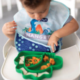 A child in a high chair uses Chewtensils, a Silicone Grip Dish with dino-shaped food, and wears a Hangry dinosaur bib from Bumkins.