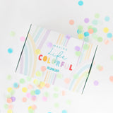 Surrounded by pastel confetti, the Bumkins Ultimate Gift Set - Ocean Life & Whale Tail features a Silicone First Feeder. The package is a white box adorned with colorful pastel stripes and the words Making Life Colorful Bumkins, adding charm to any meal.