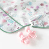 Pastel pink Chewtensils with the Ultimate Gift Set - Floral & Lace SuperBib by Bumkins on a white surface.