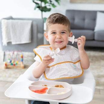 Smiling toddler in a highchair, using Bumkins Ultimate Gift Bundle, Desert Boho for self-feeding with ease.