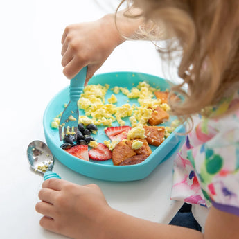 Child enjoying eggs, berries & sweet potatoes from a food-safe Bumkins Silicone Grip Plate: Blue with secure suction base.