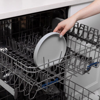 Person placing a Bumkins Silicone Grip Plate: Gray in the dishwasher, securing it with its food-safe silicone base.