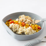 Bumkins Silicone Grip Plate: Gray, filled with shredded chicken, corn, cherry tomatoes, mashed potatoes; gray-handled fork and spoon nearby.