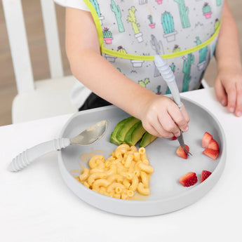 Child enjoying macaroni, strawberries, and avocado from a Bumkins Gray Silicone Grip Plate with food-safe suction base.