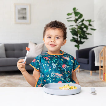 A smiling child with a fork enjoys scrambled eggs on the Silicone Grip Plate: Gray by Bumkins, ensuring no spills.