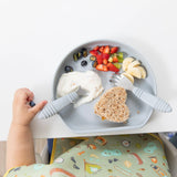 A childs hand reaches for blueberries on a Bumkins Silicone Grip Plate: Gray, filled with yogurt, fruit, and a sandwich, secured by suction.