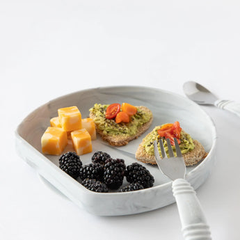 Silicone Grip Plate: Marble by Bumkins with cubed cheese, avocado toast with cherry tomatoes, blackberries; fork and knife nearby.