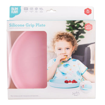 A child enjoys using the Bumkins Silicone Grip Plate in pink, designed for ages 6+ months with a food-safe silicone suction base.