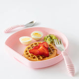 Bumkins Silicone Grip Plate in Pink features waffles, strawberries, eggs, and kiwi, with a fork & spoon on a white background.