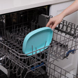 A hand places a Bumkins Silicone Grip Tray: Blue into an open dishwasher.