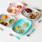 Bumkins Silicone Grip Tray: Blue holds four colorful plates with assorted healthy foods for kids on a white background.