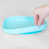 A hand lifts the edge of a Bumkins Silicone Grip Tray: Blue with a suction base on a light surface.