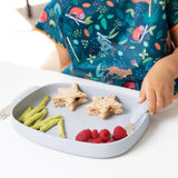 A child loves star sandwiches, green snacks, and raspberries on a gray Bumkins Silicone Grip Tray with a food-safe suction base.