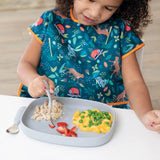 A child enjoys chicken, strawberries, and macaroni with peas from a Bumkins Silicone Grip Tray: Gray on a strong suction base bib.