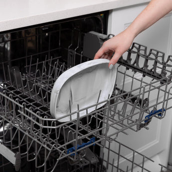 A hand placing a Bumkins Silicone Grip Tray: Marble in the top rack of an open dishwasher.