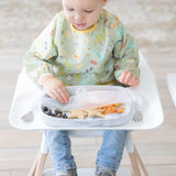 A toddler in a highchair enjoys blueberries and shaped bread from a Bumkins CPSIA-compliant Silicone Stretch Lid Grip Dish.