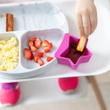 Child dips breadstick in sauce with scrambled eggs. Strawberries and lollipop-colored dish on tray, featuring Bumkins Silicone Little Dipper.