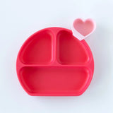 A red silicone Bumkins plate features three sections and includes a pink heart-shaped reusable condiment cup.