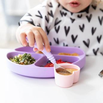 Child enjoys treats from a Bumkins Silicone Little Dipper in Lollipop colors, while wearing a shirt with heart patterns.