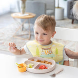 A toddler smiles at a table, enjoying snacks with a fork from colorful Bumkins Silicone Little Dipper 3-Pack in Tutti-Frutti.