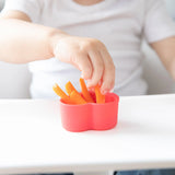 A child eagerly reaches for carrot sticks in a red Silicone Little Dipper by Bumkins, discovering fun shapes and colors on the table.