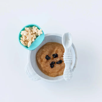 A white bowl of applesauce with raisins sits beside a blue star cereal dish, both on Bumkins Silicone Little Dipper set: Gumdrop.