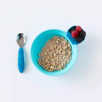 A blue cereal bowl with Bumkins Silicone Little Dipper holders for berries sits next to a spoon with a blue handle on a white background.