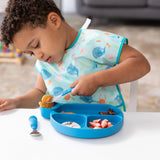 A child in a bib enjoys strawberries from a safety-tested Bumkins Silicone Little Dipper, using a fork and spoon with ease.