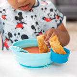 A child in a Mickey Mouse shirt happily dips breadsticks into soup from Bumkins Silicone Little Dipper, Gumdrop 3-Pack for peace of mind.