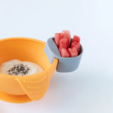 Yellow bowl with yogurt and chia seeds, plus a Bumkins gray Silicone Little Dipper holding watermelon on a white background.