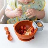 Child in a high chair, enjoying strawberries and bananas with Bumkins Silicone Little Dipper Round 3-Pack: Taffy for peanut butter.