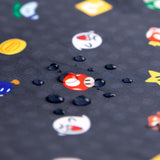 Close-up of water droplets on the Bumkins Splat Mat: Super Mario™ Lineup, featuring cartoon mushrooms and stars on a dark background.