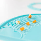 The blue Silicone Sensory Placemat by Bumkins, with food crumbs and bits scattered on it.