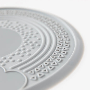 Close-up of Bumkins Silicone Sensory Placemat: Gray, featuring a circular pattern with textured dots and triangles on a nonslip surface.