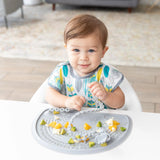 A baby enjoys sensory play with a beaded toy on a Bumkins Silicone Sensory Placemat: Gray, while wearing a bib in the high chair.