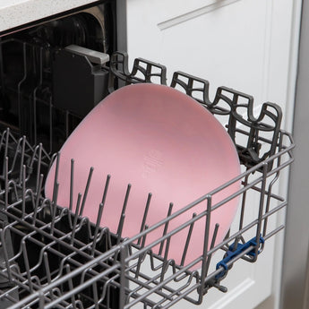 A Silicone Sensory Placemat: Pink by Bumkins is on the top rack of an open dishwasher.