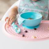 Baby exploring sensory play with food in a high chair, using a blue bowl and spoon on a Bumkins Silicone Sensory Placemat: Pink.