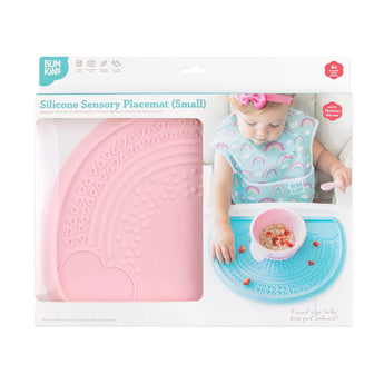 A baby explores a blue sensory placemat with a bowl; the packaging features Bumkins Pink Silicone Sensory Placemat.