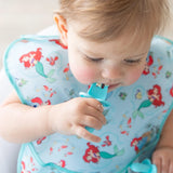 Toddler in Ariel-themed Bumkins SuperBib®, holding a turquoise waterproof pacifier clip.