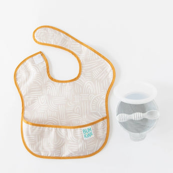 Bumkins SuperBib® 3 Pack: Desert Boho bib with orange trim, next to a grey bowl and utensils on a white background.