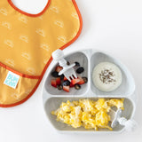 A SuperBib® from Bumkins Desert Boho collection sits beside a sectioned plate of scrambled eggs, fruit, and chia seed yogurt.