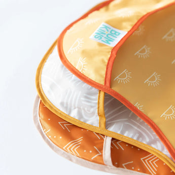 Close-up of Bumkins SuperBib® 3 Pack: Desert Boho featuring orange, yellow, and white geometric and sun patterns.