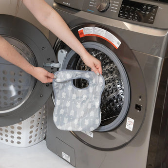 A person loads their waterproof Bumkins SuperBib®: Arrow into a front-loading washing machine.