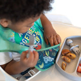 Toddler in a high chair wearing Bumkins SuperBib® 3 Pack: All Together Now, using a utensil, eating from a divided plate.